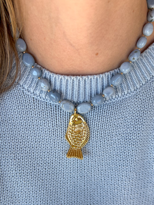 Necklace with blue beads and a gold fish pendant on a light blue sweater.